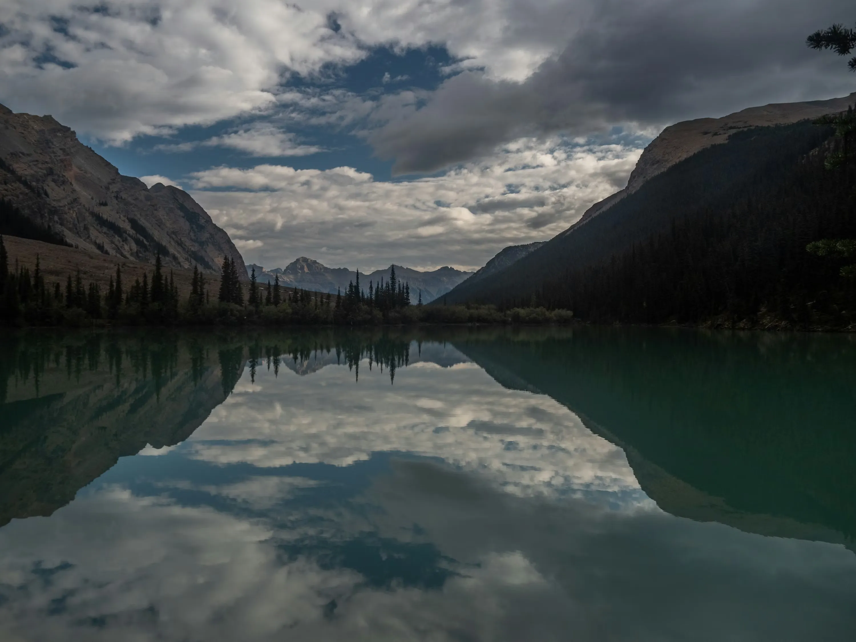 Calm natural landscape with mountains, evergreen trees, and a peaceful lake reflecting the sky